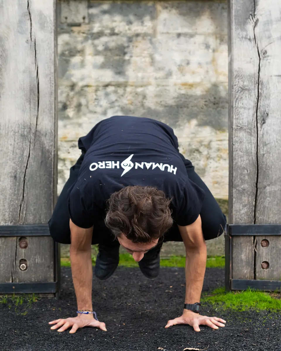 Coach sportif en équilibre sur les mains, posture du corbeau, devant un mur en pierre