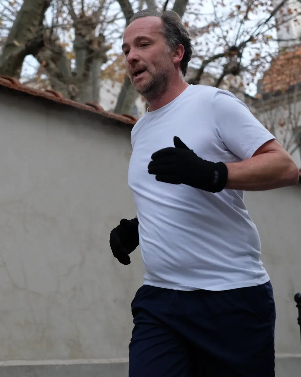 Homme d'une quarantaine d'années courant le long d'un mur, dans une rue calme