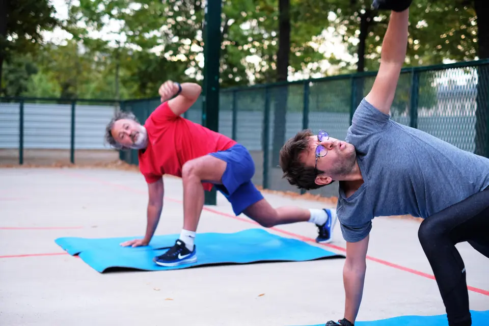 Deux hommes, dont un senior, en rotation du buste sur des tapis, sur un terrain de sport